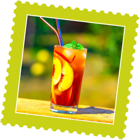 A refreshing drink with ice, garnished with mint and peach slices, served in a tall glass against a blurred outdoor background.