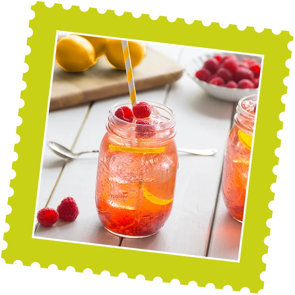 Two mason jars of refreshing raspberry lemonade with lemon slices and raspberries on top, set on a table with lemons and raspberries nearby.