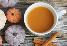 A warm cup of spiced beverage surrounded by small pumpkins and cinnamon sticks on a rustic wooden surface.