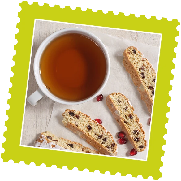A cup of tea next to four pieces of biscotti and a few scattered pomegranate seeds on parchment paper.